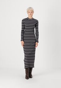 Vestido de manga longa e nervurado com riscas horizontais pretas e cinzentas, com um decote redondo e uma abertura lateral, usado com botas castanhas.