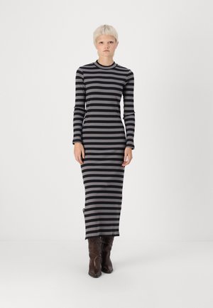 Long-sleeve, ribbed dress featuring horizontal black and gray stripes, with a round neckline and a side slit, worn with brown boots.