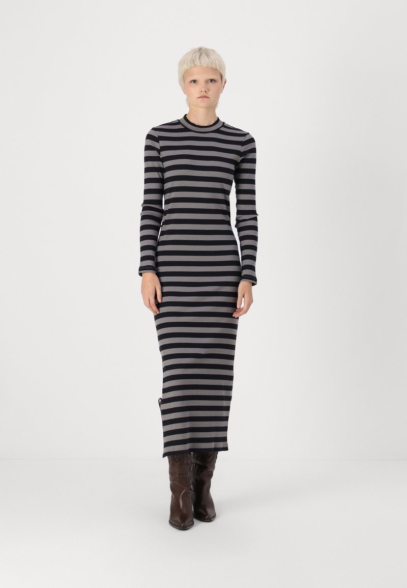 Vestido de manga longa e nervurado com riscas horizontais pretas e cinzentas, com um decote redondo e uma abertura lateral, usado com botas castanhas.