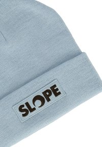 Ljusblå stickad mössa med vik, prydd med en rektangulär lapp med ordet "SLOPE" i mörkbrunt. Texturerad yta.