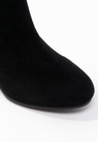 Bottine en daim noir avec bout arrondi, texture lisse, et semelle basse et unie noire. Design simple sans éléments métalliques visibles.