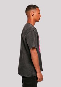 Oversized black cotton t-shirt with short sleeves, distressed texture, featuring a large pink graphic print on the front. Straight hem.