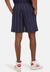 Pantaloni corti a righe blu navy con strisce verticali bianche e rosse, vita elasticizzata, tessuto morbido e vestibilità comoda, abbinati a sneaker alte.