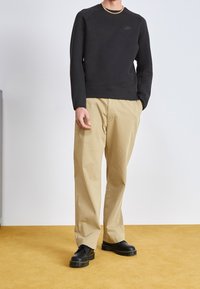 Svart sweatshirt med rund halsringning och långa ärmar, kombinerad med beige vida byxor och svarta snörskor. Guldkedja som syns som accessoar.