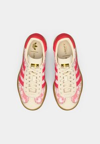 Adidas sneakers featuring a cream leather upper with pink floral patterns, three pink stripes, and white laces. Rubber gum outsole.