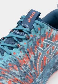 Chaussure de course Asics avec un dessus texturé turquoise et des accents orange, des lacets plats et une languette rembourrée pour le soutien.