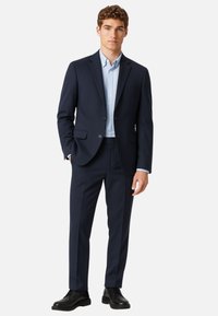 Abito blu navy con vestibilità su misura, pantaloni abbinati e camicia da uomo azzurro chiaro. Tessuto morbido, rever standard e eleganti scarpe nere.