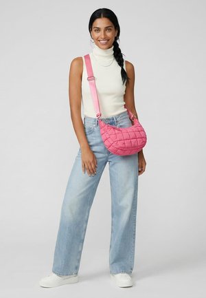 Woman with braided hair wearing sleeveless white turtleneck, light blue jeans, white sneakers, and carrying a pink quilted shoulder bag.