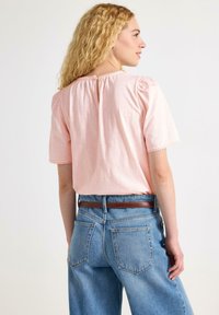 Helles rosa Kurzarm-Oberteil mit gerafftem Halsausschnitt und Spitzenbesatz an den Ärmeln, kombiniert mit hochgeschnittenen blauen Jeans.
