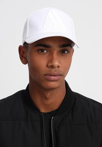 Cappellino bianco da baseball con logo in rilievo "AX", realizzato in materiale sintetico liscio. Presenta una visiera curva e una chiusura regolabile sul retro.