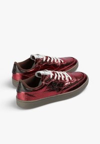 Zapatillas metálicas rojas con superficie texturizada, cordones blancos, interior marrón y suela de goma gris; con un logo de calavera negra.