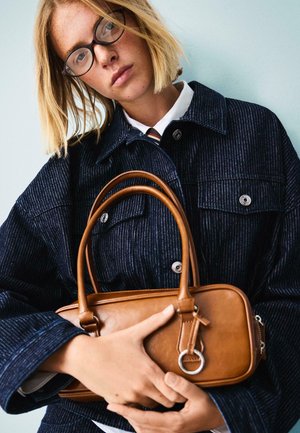 Sac à main en cuir marron avec des poignées arrondies, de forme rectangulaire, texture subtile et accent en métal argenté. Porté avec une veste à rayures bleu marine.