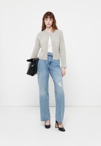 Lys grå strikkegenser med rund hals og frontlommer, kombinert med revne blå jeans og svarte spisse hæler, holder en svart veske.