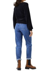 Schwarzer Fleece-Pullover, blaue Jeans mit Umschlägen und braune Knöchelstiefel mit elastischen Seiteneinsätzen, von hinten betrachtet.