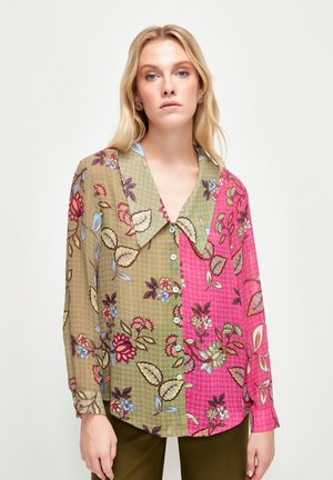 Chemise à motifs floraux avec un col. Côté gauche en olive clair avec des fleurs multicolores ; côté droit en rose vif. Manches longues.