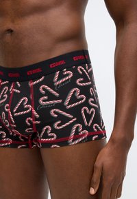 Μαύρα ανδρικά μποξέρ με παιχνιδιάρικα σχέδια κόκκινων και λευκών καρδιών καραμέλας. Διαθέτουν αντίθετη κόκκινη ζώνη μέσης με το λογότυπο "Diesel".
