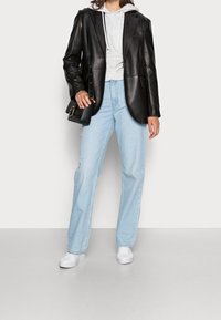 Blazer di pelle nera su felpa grigia, abbinato a jeans azzurri chiari e sneakers bianche. Il modello porta una piccola borsa nera.