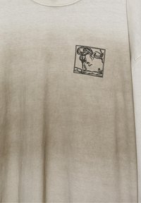 Vaaleabeige collegepaita, jossa on pieni musta viivapiirros tanssivasta ihmisestä ja puusta rintataskualueella.