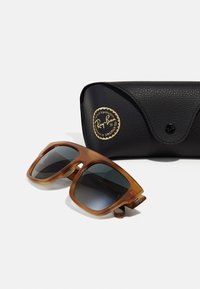 Ochelari de soare Ray-Ban cu ramă din tortoiseshell de culoare maro deschis, lentile întunecate și un etui texturat negru cu un logo auriu.
