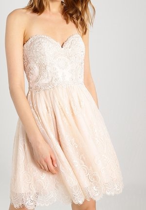 Trägerloses, blassrosa Spitzenkleid mit figurbetontem, besticktem Oberteil und ausgestelltem Rock, getragen von einer Frau mit offenen braunen Haaren.