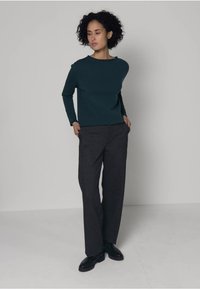 Haut vert foncé à manches longues associé à un pantalon gris à jambes larges. Le haut présente un col bateau ; le pantalon a une texture lisse et tombe jusqu'au sol.