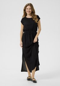Black maxi dress with short sleeves, drawstring waist, and side slit. Lightweight fabric drapes softly, creating a relaxed silhouette.