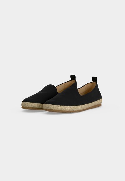 Paire d'espadrilles noires sans lacets avec semelle en jute tissée et intérieur beige sur un fond uni clair.