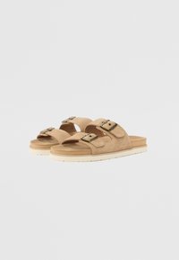 Sandales en suède beige avec deux sangles réglables dotées de boucles en métal, une semelle rembourrée et une semelle extérieure légère en caoutchouc blanc.