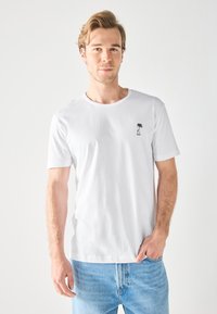 Witte T-shirt met korte mouwen, gemaakt van katoen, met een ronde halslijn en een kleine zwarte palmboom grafiek op de linker borst.