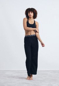 Zwarte sportieve cropped tanktop met wijde zwarte broek met een merk-elastische tailleband. Soepele textuur, ontspannen pasvorm en minimalistisch design.