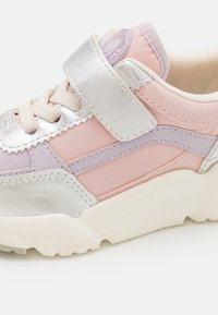 Zapatilla con una parte superior de cuero plateado, paneles en rosa y lavanda, superficie texturizada y una correa de velcro; suela blanca gruesa para soporte.