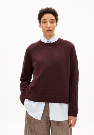 Pull marron à col rond, avec un ourlet et des poignets côtelés, et des manches raglan, superposé à une chemise col bleu clair. Tissu texturé.