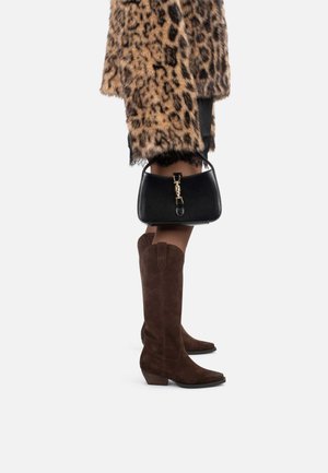 Bottes en suède marron jusqu'au genou avec un bout pointu et un talon bas, associées à un manteau en fausse fourrure à imprimé léopard et un sac à main noir.