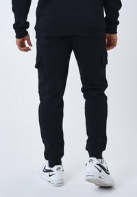 Joggers de cargo negros con bolsillos laterales, piernas ajustadas y puños elásticos, combinados con zapatillas Nike blancas con un swoosh negro.