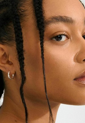 Silver hoop earring with a twisted design, set against skin with braided hair, showcasing a smooth, even texture.
