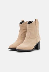 Semišové kotníkové boty v světlé béžové barvě s špičatou špičkou a blokovým podpatkem o výšce 3 palce. Mají poutka na natahování a šití pro detaily.