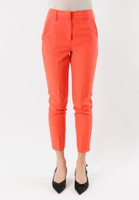 Pantaloni rossi su misura con una finitura liscia, caratterizzati da una gamba affusolata e tasche laterali. Abbinati a décolleté nere a punta.