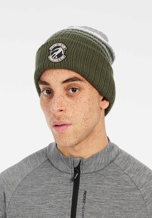 Green knitted beanie with gray and white stripes, featuring a round logo patch. Ribbed texture, form-fitting design, and soft fabric.
