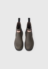 Bottes de cheville en caoutchouc marron foncé avec des panneaux latéraux élastiques, un bout rond et une semelle noire. Présente un label logo rouge et blanc sur le devant.