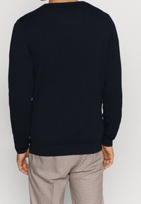 Marineblauer Pullover aus strukturiertem Strick, mit Rundhalsausschnitt und gerippten Bündchen. Getragen mit karierten Hosen.