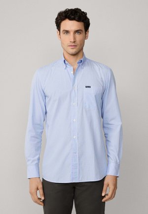 Helles blaus gestreiftes Button-up-Hemd mit einer Brusttasche, abgerundetem Saum und langen Ärmeln. Auf der linken Seite befindet sich ein kleines Markenlabel.
