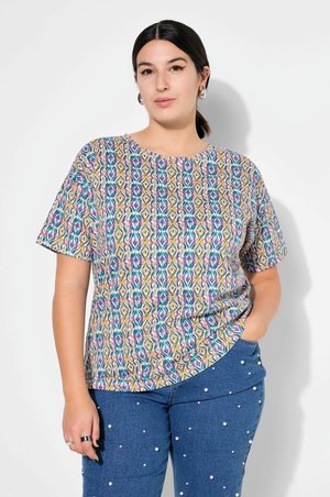 T-shirt z krótkim rękawem, z wielokolorowym geometrycznym wzorem w odcieniach purpurowym, turkusowym, pomarańczowym i żółtym, w połączeniu z niebieskimi dżinsami ozdobionymi białymi perłami.