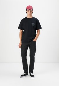 Camiseta de algodón negra de manga corta, con un gráfico en el pecho. Combinada con jeans de mezclilla oscura y zapatillas negras con cordones blancos.