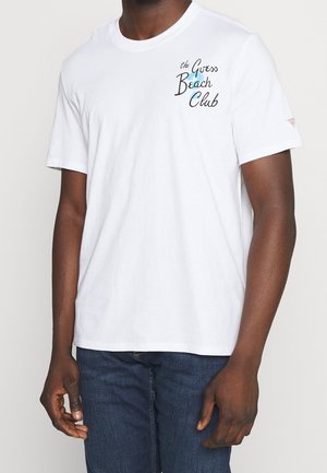 Weißes Baumwoll-T-Shirt mit einem bedruckten Logo "the Guess Beach Club" in Schwarz und Türkis, mit kurzen Ärmeln und Rundhalsausschnitt.
