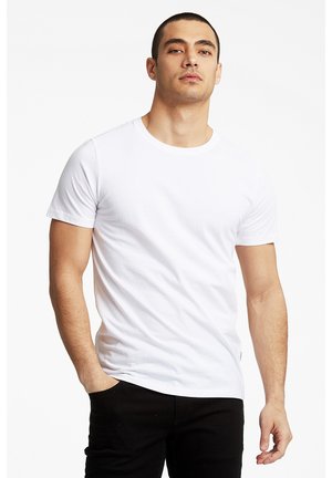 Vit bomull t-shirt med rund hals, korta ärmar och rak passform, i kombination med svarta jeans. Slät textur, minimalistisk design.