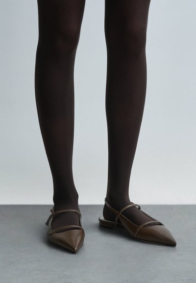 Ruskeat nahkaiset ballerinat, joissa on kärjellinen pää, ja kaksi remmiä jalan päällä, yhdistetty läpinäkymättömiin mustiin sukkahousuihin. Tasainen korko, minimalistinen muotoilu.