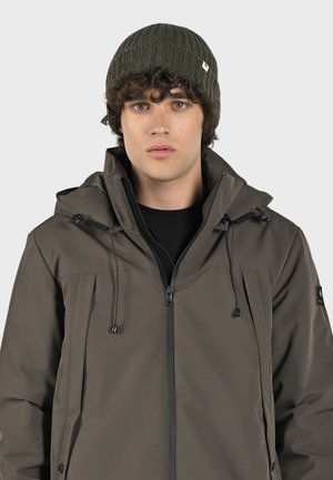 Dark brown jacket with a zip closure, adjustable drawstring hood, and black accents. Wearer has a ribbed dark green beanie.
