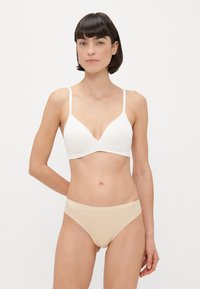 Valge rinnahoidja sügava dekoltee ja õhukeste rihmadega, koos nude värvi õmblusteta aluspükstega. Mõlemad esemed on sujuva, minimalistliku disainiga.