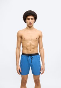 Μπλε μαγιό σορτς από ελαφρύ ύφασμα με μαύρη ελαστική μέση και κορδόνι, με μικρό λογότυπο στο πλάι.