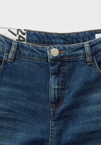 Denimspijkerbroek met een donkerblauwe wassing, voorzien van koperen stiksels, een metalen knoopsluiting en een verstelbare tailleband met een logo label.